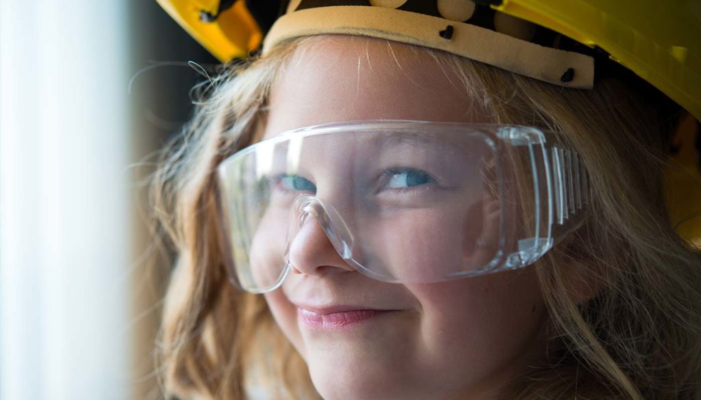 close up of a little girl wearing safety glasses and a hard hat