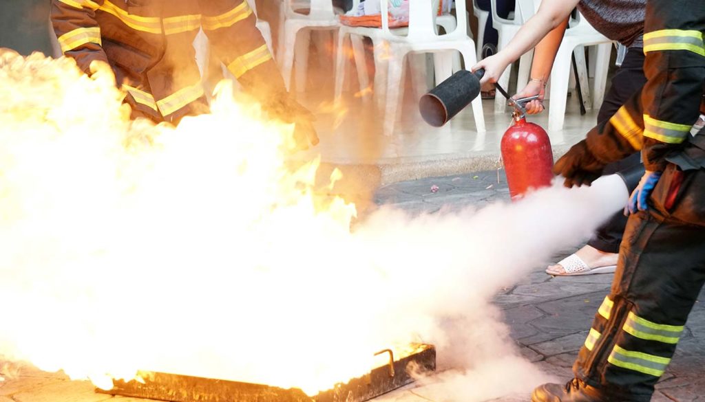 woman practicing fire extinguisher with firefighters nearby