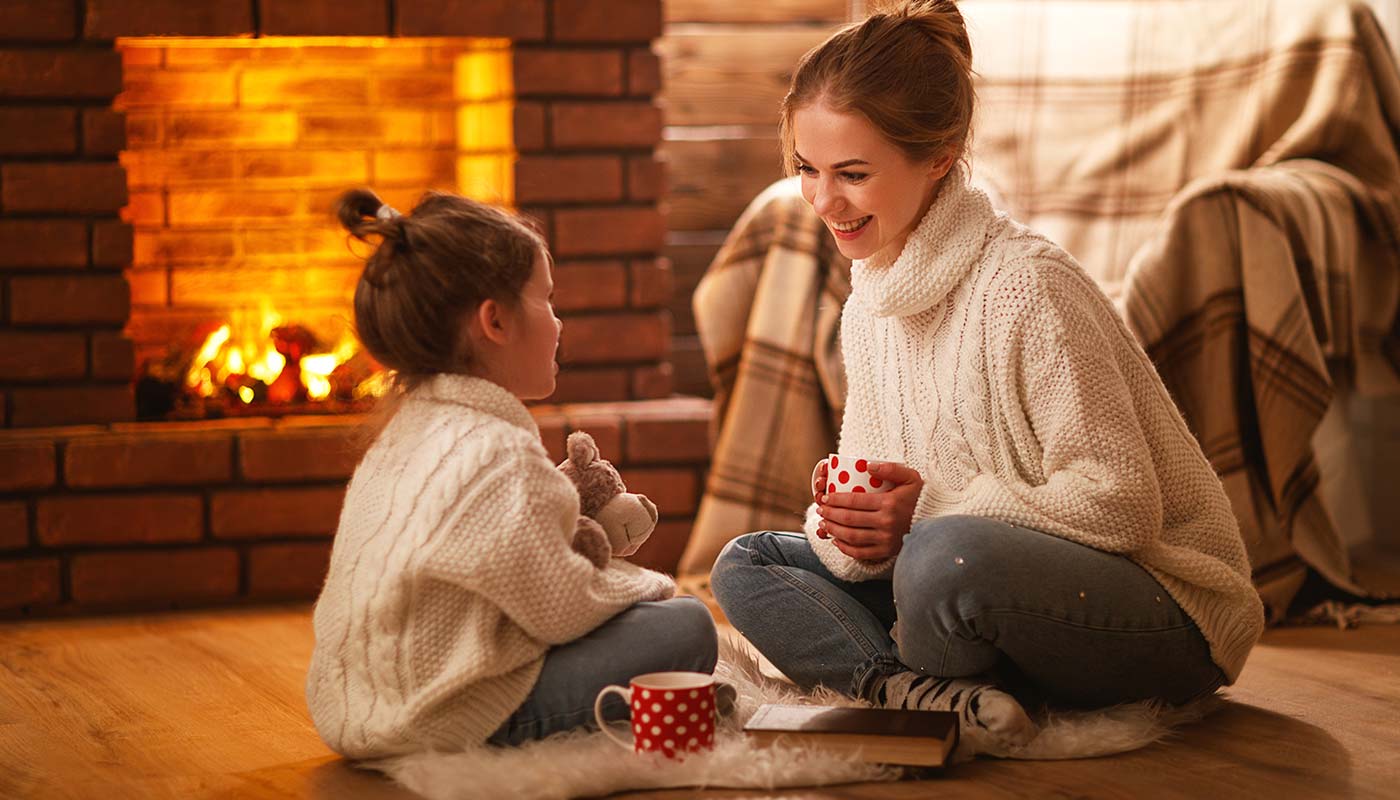 mother and daughter having hot cocoa together near the fireplace
