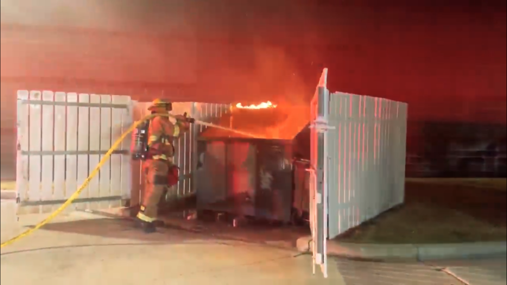 firefighter spraying dumpster fire with hose