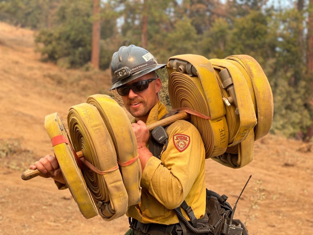 wildland firefighter carrying rolled hose line